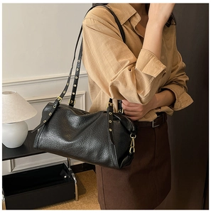 Close-up of black leather shoulder bag featuring golden eyelet straps and metal buckle details