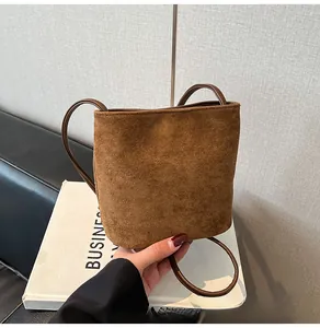 Sac seau minimaliste en daim marron avec fine bandoulière tenu à la main