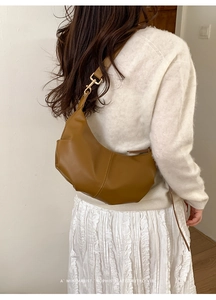 Detail of tan crescent shoulder bag featuring fine vertical stitching and retro design