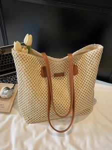 Large beige woven straw tote bag with brown PU straps on a modern workspace desk