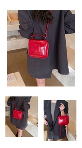 Detail view of red glossy oil wax leather handbag with square buckle and top handle