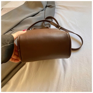 Detail showing the rounded bottom design and adjustable leather strap of the brown bag