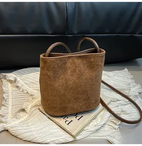 Détail du sac seau en daim marron mat avec poignée supérieure et fine bandoulière