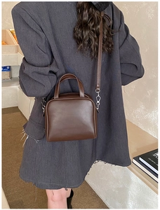 Model wearing a dark brown leather box bag with dual handles and silver metal hardware