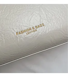 Close-up of white wrinkled leather bag showing golden Fashion & Bags logo engraving