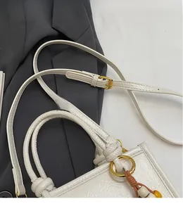Detail of white textured shoulder bag with golden rings and a long adjustable strap