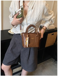 Details einer Vintage-Eimertasche aus braunem Leder mit bunten Holzperlen und Goldbeschlägen