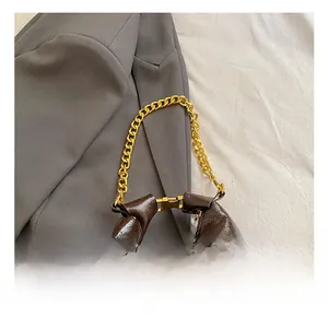 Close-up of glossy brown underarm bag featuring premium gold chain strap and buckle details