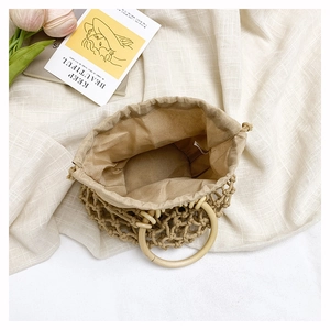 Detail of hand-woven beige bucket bag featuring wooden handle and drawstring liner