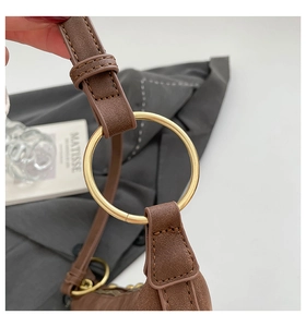 Détail de l'anneau métallique doré et des coutures sur un sac en cuir marron