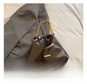 Macro detail of the dark coffee oil wax leather texture and golden chain on the bag