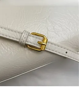 Macro shot of gold metal buckle and wrinkled leather texture on cream crossbody bag
