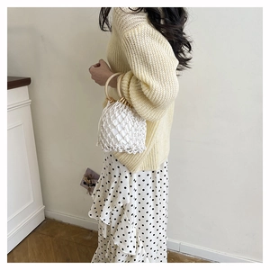 Detail showing white woven bucket bag with light round wood handle and drawstring lining