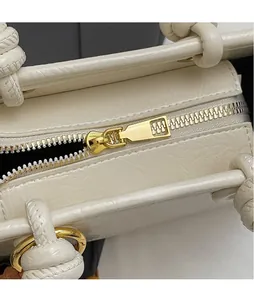 Detail of white embossed leather bag with golden hardware zipper and knotted handle