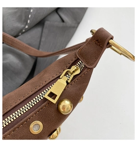 Détail d'un sac à bandoulière marron avec rivets dorés et fermeture éclair en métal lisse