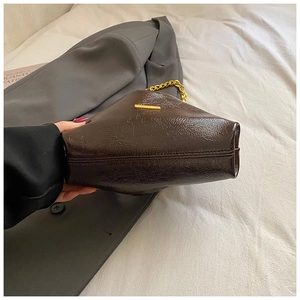 Detail of dark brown oil wax leather bag featuring a chunky gold chain and metal bar