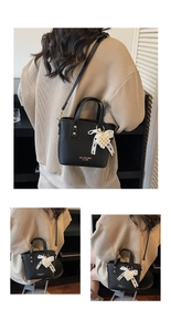 Detail of black pebbled leather handbag with lace bow and heart pearl pendant