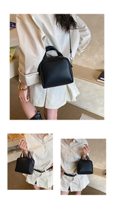 Detail view of the sleek black leather handbag being worn as a crossbody and top handle bag