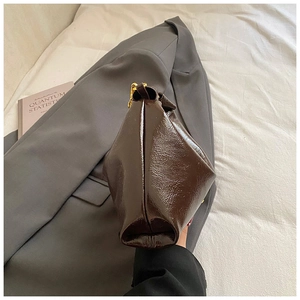 Detail of dark brown glossy patent leather bag with gold chain and side pleat design