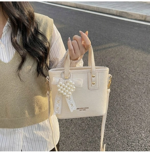 Detail of cream white bucket bag with pearl heart charm and lace bow on textured leather