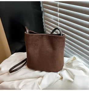 Détail d'un sac seau en daim marron givré avec une bandoulière minimaliste en cuir souple