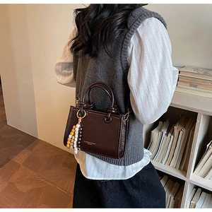 Detail of dark brown leather tote with fashion lettering and beaded ethnic bag charm
