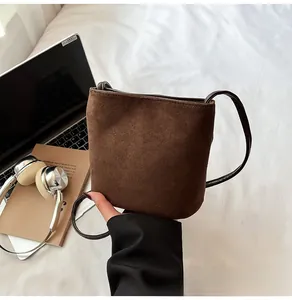 Gros plan du sac seau en daim marron avec fine bandoulière posé sur un bureau de travail
