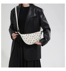Sac bandoulière demi-lune blanc clouté or, porté par un mannequin en veste de cuir