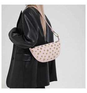 Détail d'un sac demi-lune rose à rivets dorés sur une veste en cuir noir