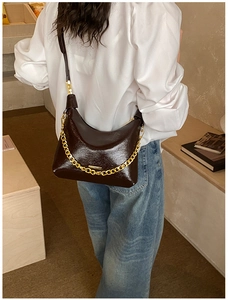 Detail of dark brown patent leather hobo bag with thick gold chain and shoulder strap