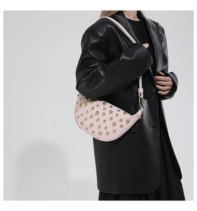 Détail du sac demi-lune rose avec rivets dorés porté sur un blazer en cuir noir