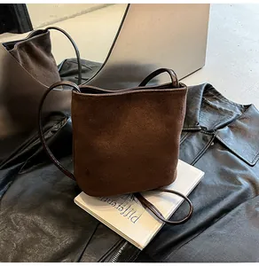 Détail d'un sac seau en daim marron au design minimaliste sur fond de cuir noir