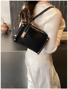 Detail of matte black leather bag with contrasting white stitching and gold metal hardware