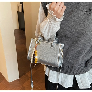 Detailed view of metallic silver pleated handbag featuring a colorful beaded pendant charm