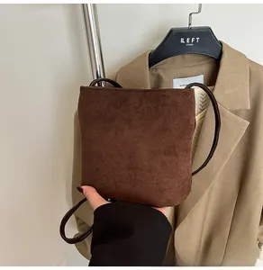 Détail d'un sac à bandoulière en cuir mat marron foncé porté avec un blazer kaki chic