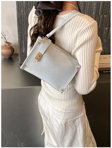 Detail of light blue glossy leather crossbody bag with gold buckle on a model