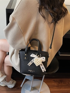 Chic black lychee leather bucket bag with lace bow and pearl heart charm on a model