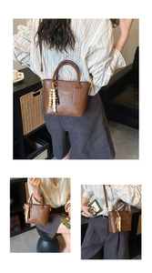 Detail of dark brown leather bucket bag featuring gold text and colorful beaded charm