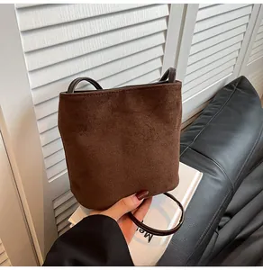 Détail d'un sac seau en daim marron mat montrant la texture douce et les fines anses
