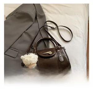 Detail of dark brown leather bowling bag with heart pendant and plush charm on grey blazer