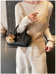 Détail d'un sac bowling noir avec un charme d'ours en peluche et une fermeture éclair