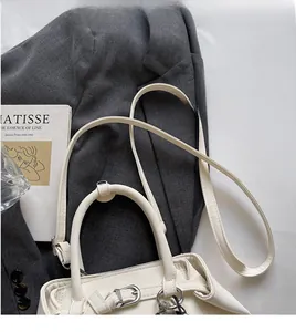 Close-up of ivory handbag with long leather strap and buckle on a grey blazer