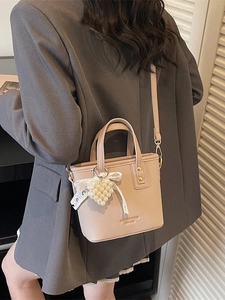 Minimalist beige pebble leather crossbody bag with pearl heart charm on a grey suit model