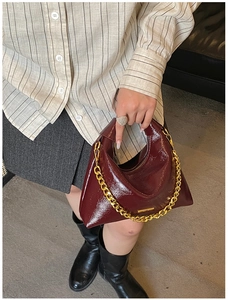 Detail of burgundy patent leather underarm bag with thick gold chain and glossy finish