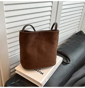 Vue détaillée du sac seau en daim marron avec fines poignées sur un livre blanc