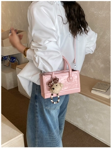 Detailed shot of a pink embossed leather handbag featuring a cute plush bear charm accessory