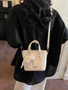 Chic beige bucket bag with pearl heart charm and lace detail on a minimalist model