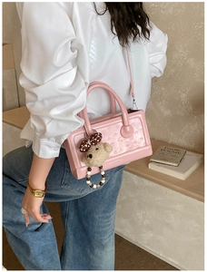 Pink rectangular handbag with embossed texture, plush bear charm, and beaded strap detail