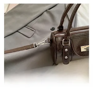 Detailed view of the silver metal hook on a dark brown glossy cylinder crossbody bag