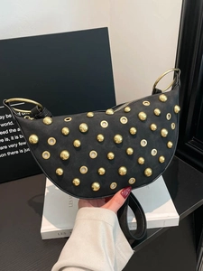 Sac croissant en daim noir avec rivets dorés et poignées en anneaux métalliques en main